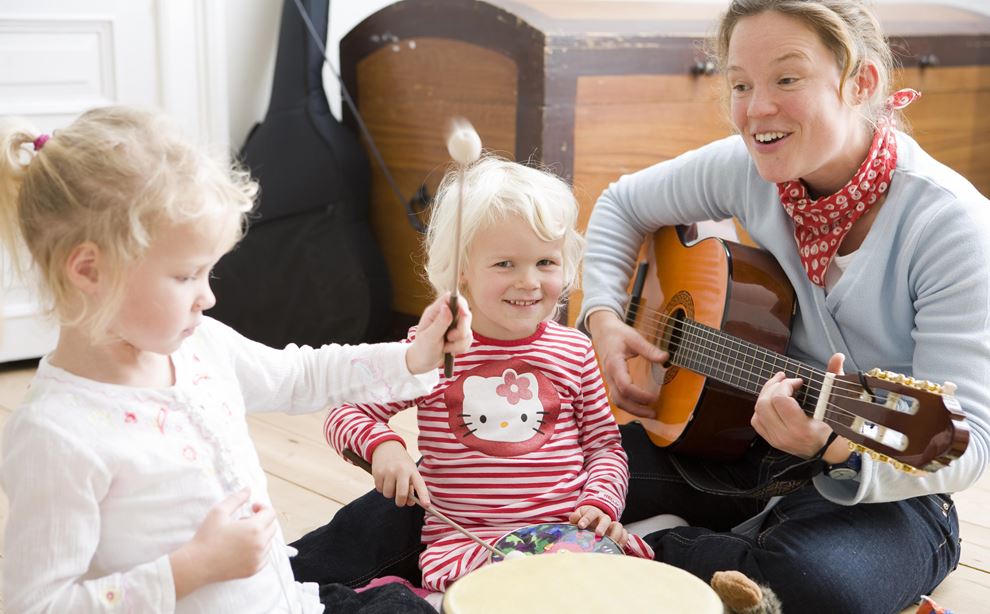 Kvinde sidder på gulvet og spiller guitar med to børn